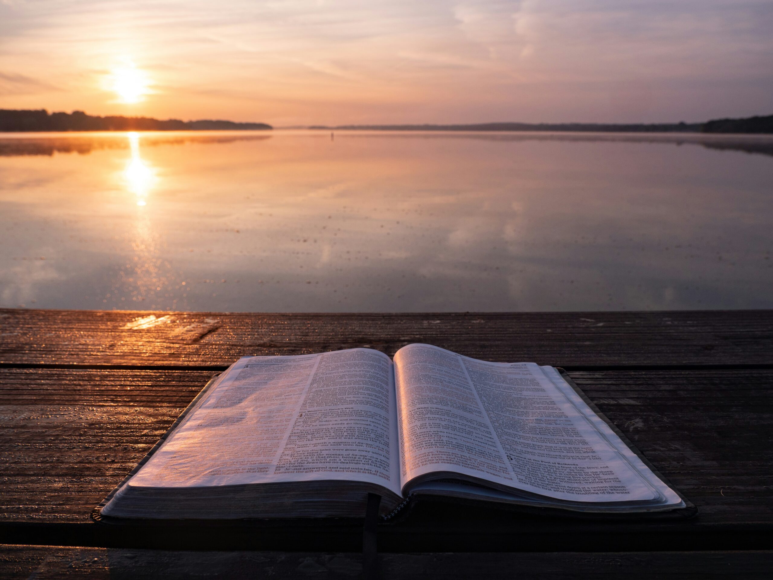 An open Bible on a wooden table at sunrise