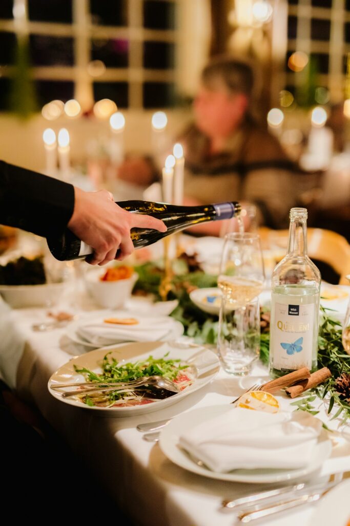 A hand pouring wine into a glass at a candlelit dinner table